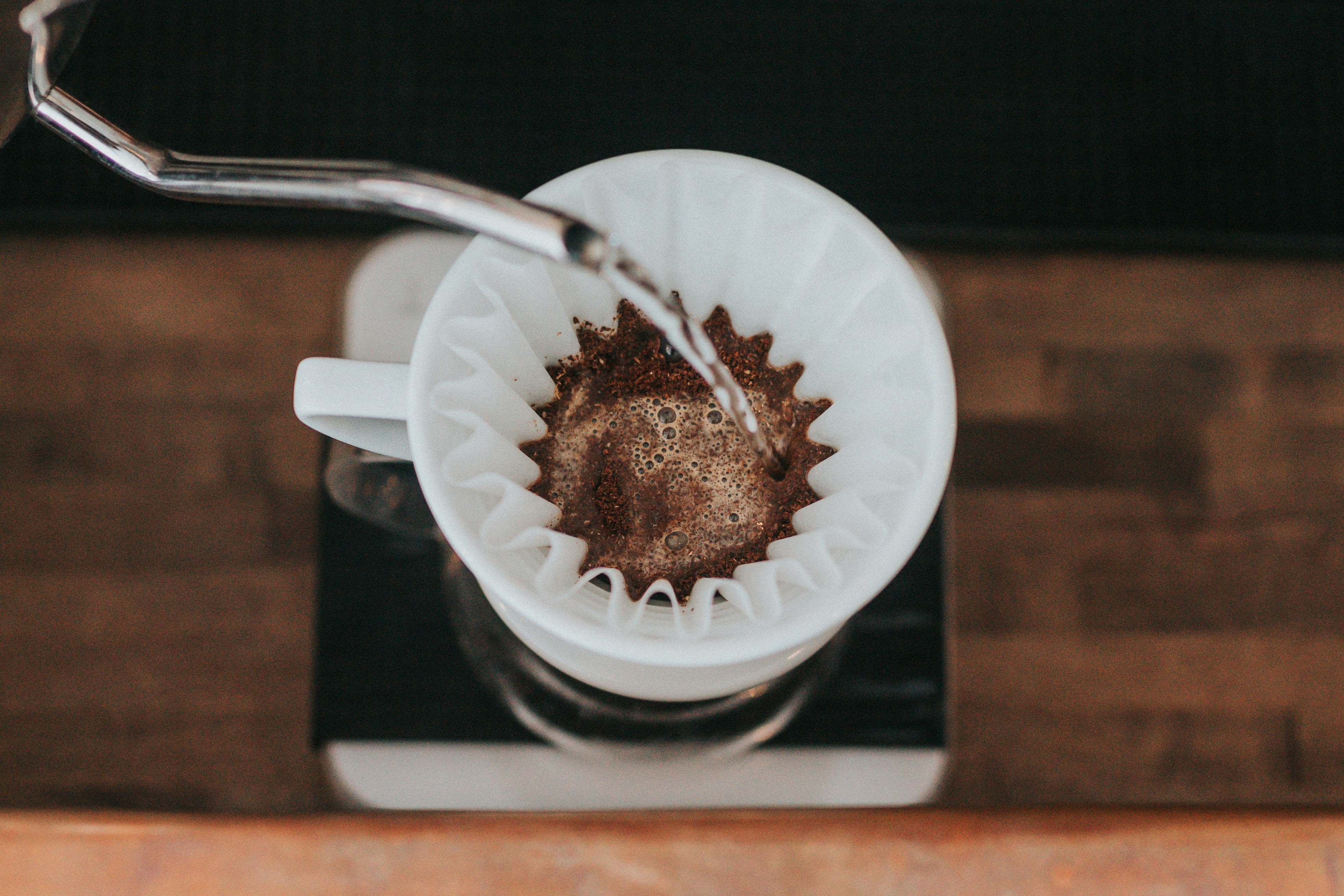 Blick von oben auf einen Kaffeefilter aus Keramik mit einer Filtertüte und Kaffee worauf Wasser gegossen wird.