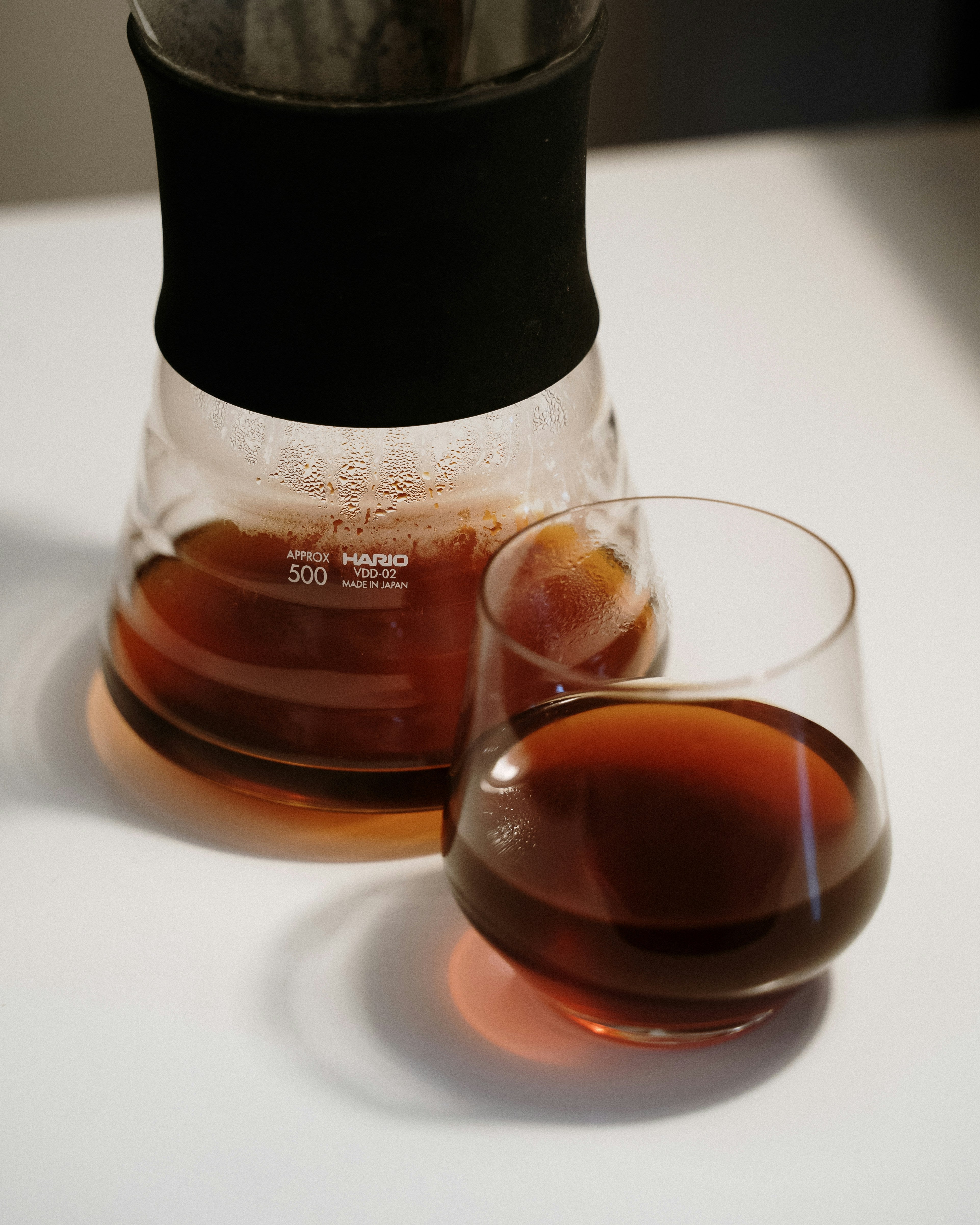 Ein Hario Glasbehälter und ein Glas stehen auf einem Tisch, in beiden Gefäßen ist heller Filterkaffee.